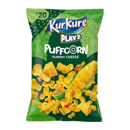 A bag of Kurkure Playz Puffcorn Yummy Cheese snack chips on a light gray background. The packaging is primarily green with a graphic of yellow corn and cheese chips.
