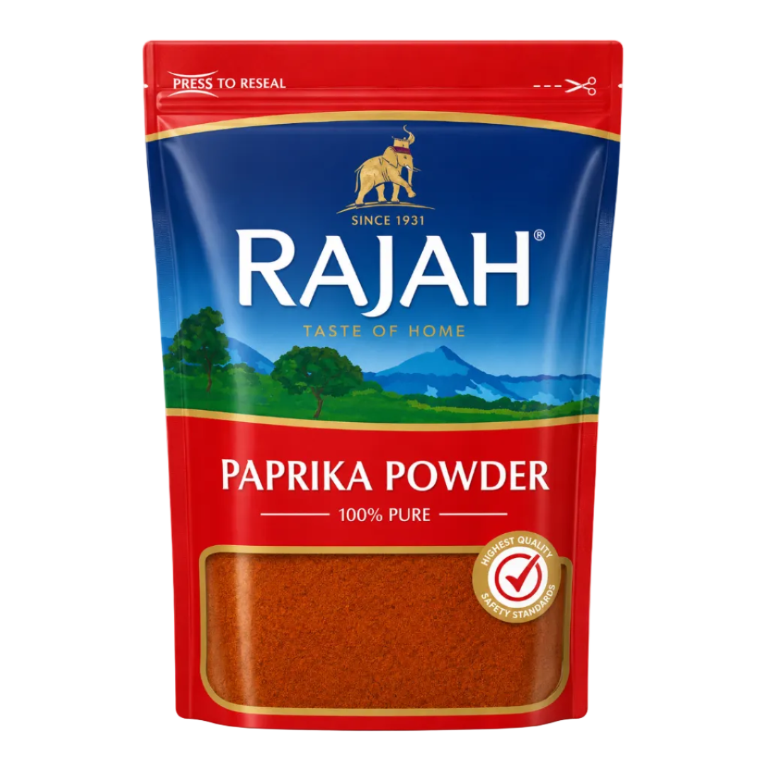 A stand-up pouch of Rajah Paprika Powder on a plain white background. The packaging is primarily red and blue with a scenic landscape illustration in the center, a clear window at the bottom showing the orange-red powder, and a gold seal indicating high quality.